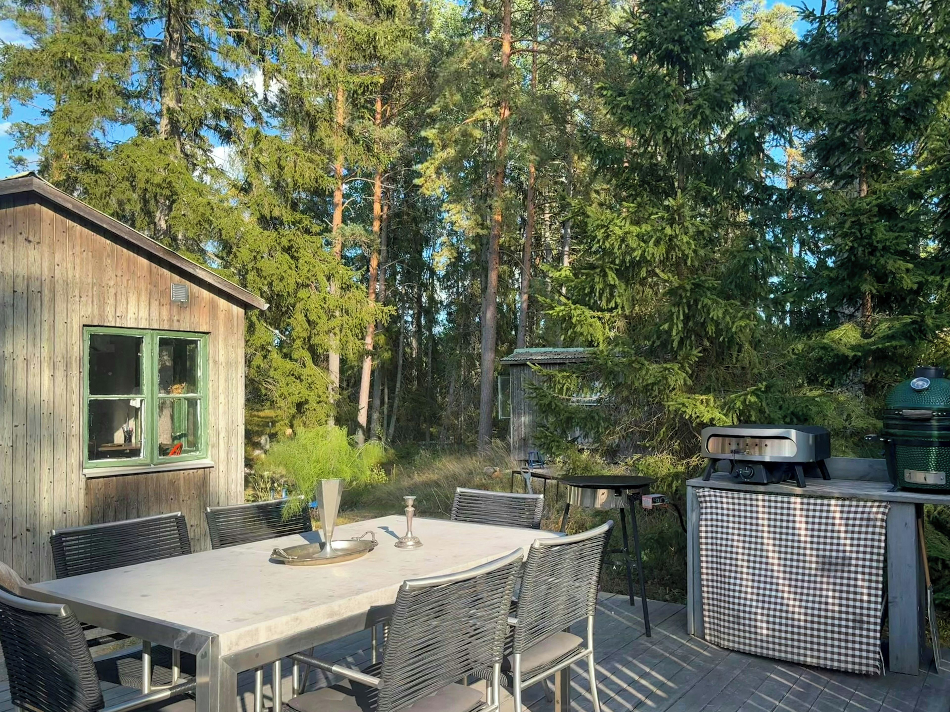A wooden cabin with a dining table and chairs, surrounded by tall trees.