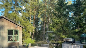 A wooden cabin with a dining table and chairs, surrounded by tall trees.