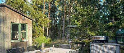 Puinen mökki, jossa on ruokapöytä ja tuoleja, ja jonka ympärillä kohoaa korkeita puita.