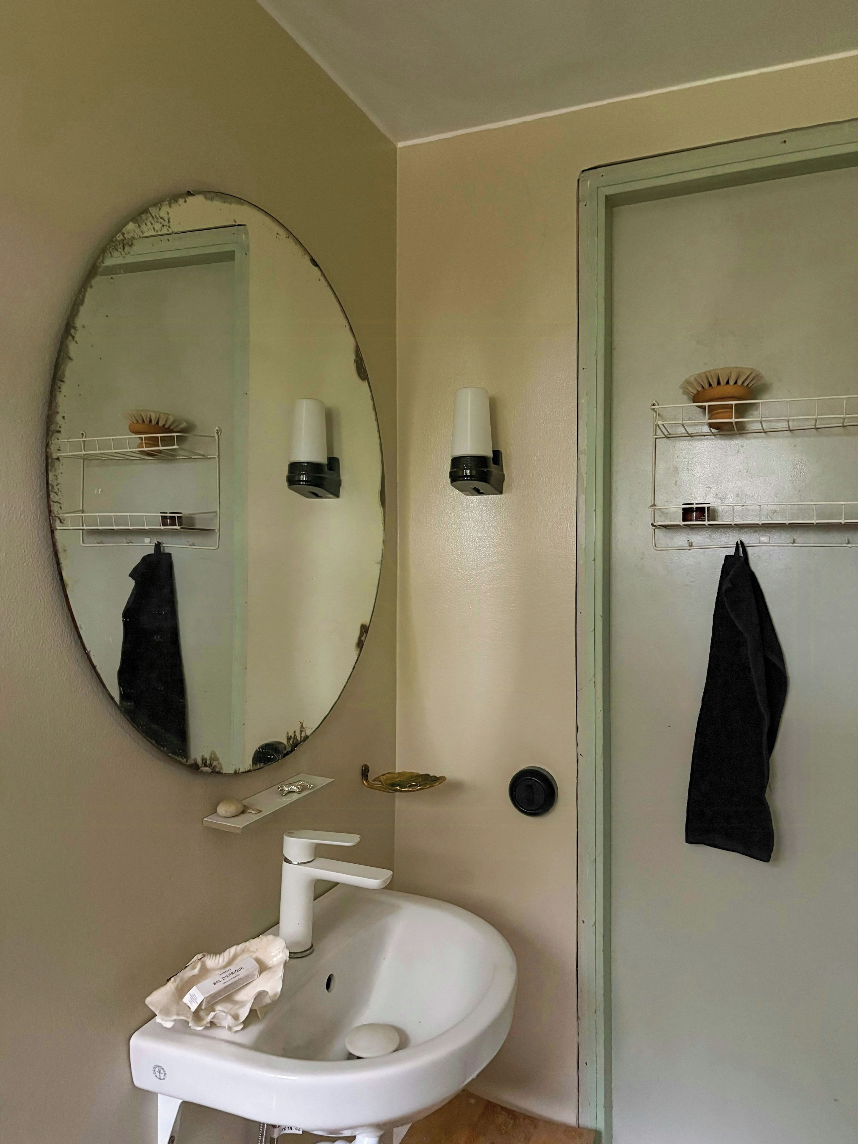 A bathroom with a round mirror, a white sink, and a towel rack.