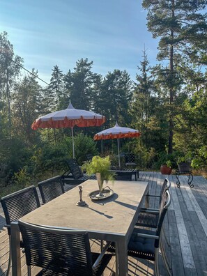 Eine Terrassenanlage im Freien mit Tisch und Stühlen, umgeben von Bäumen und zwei Sonnenschirmen.