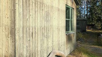 En træbygning med et vindue, en buet trækonstruktion foran og et naturligt udendørs miljø.
