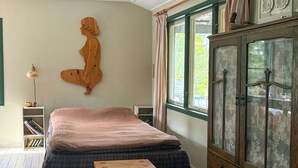 Quarto com cama, um armário de madeira, uma mesinha e uma escultura de madeira fixada na parede.