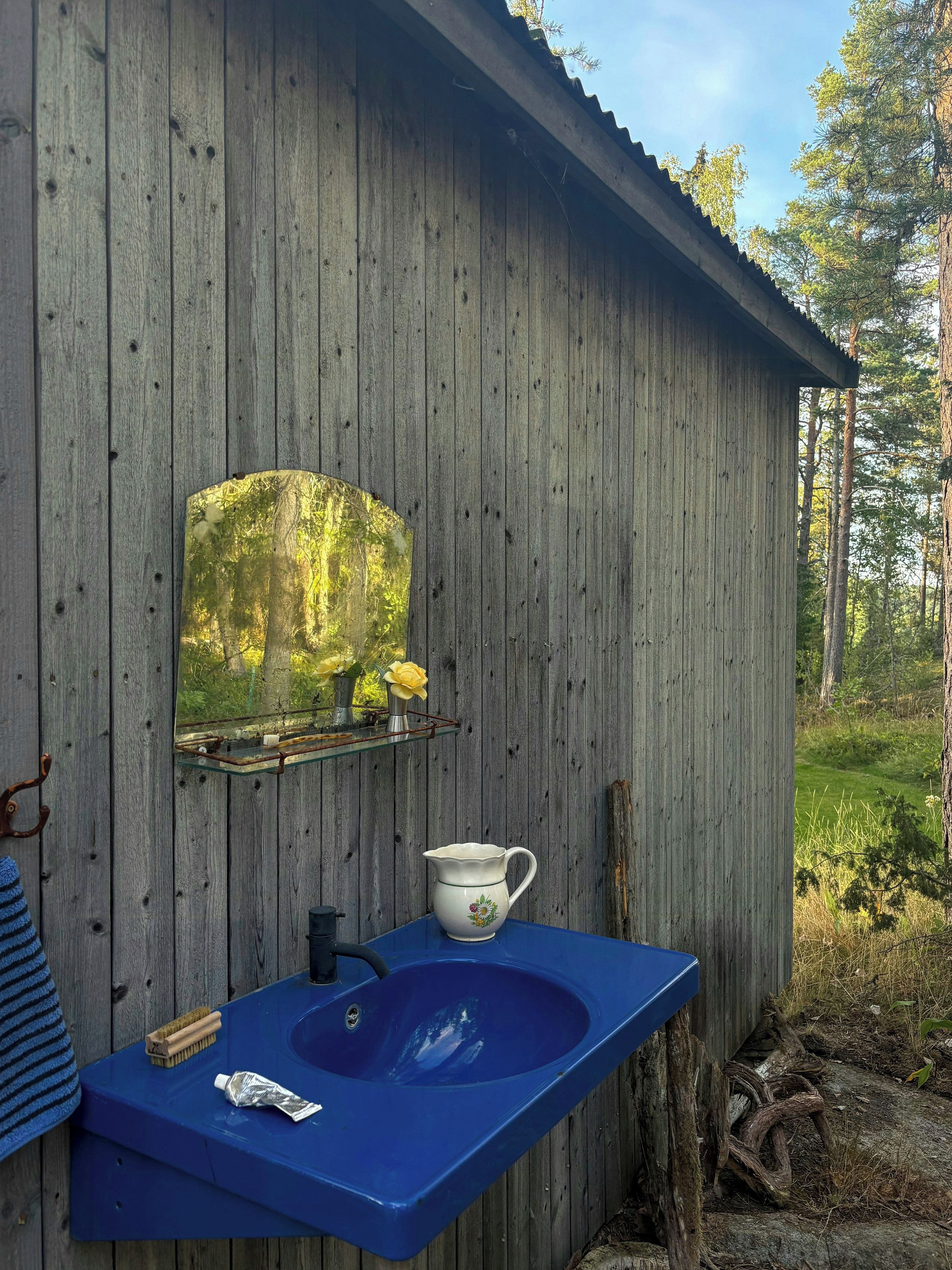 Een rustieke houten cabin met een blauwe gootsteen, een spiegel en een plank met een vaas en kan.