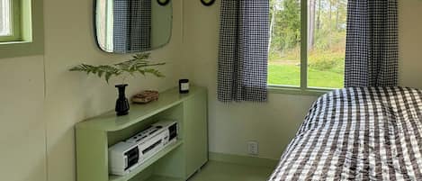 Ett sovrum med en säng, en byrå, en spegel, ett fönster med gardiner och en växt.