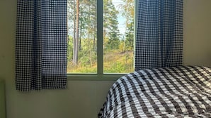 A bedroom with a checkered bedspread, a window with curtains, and a view of trees outside.