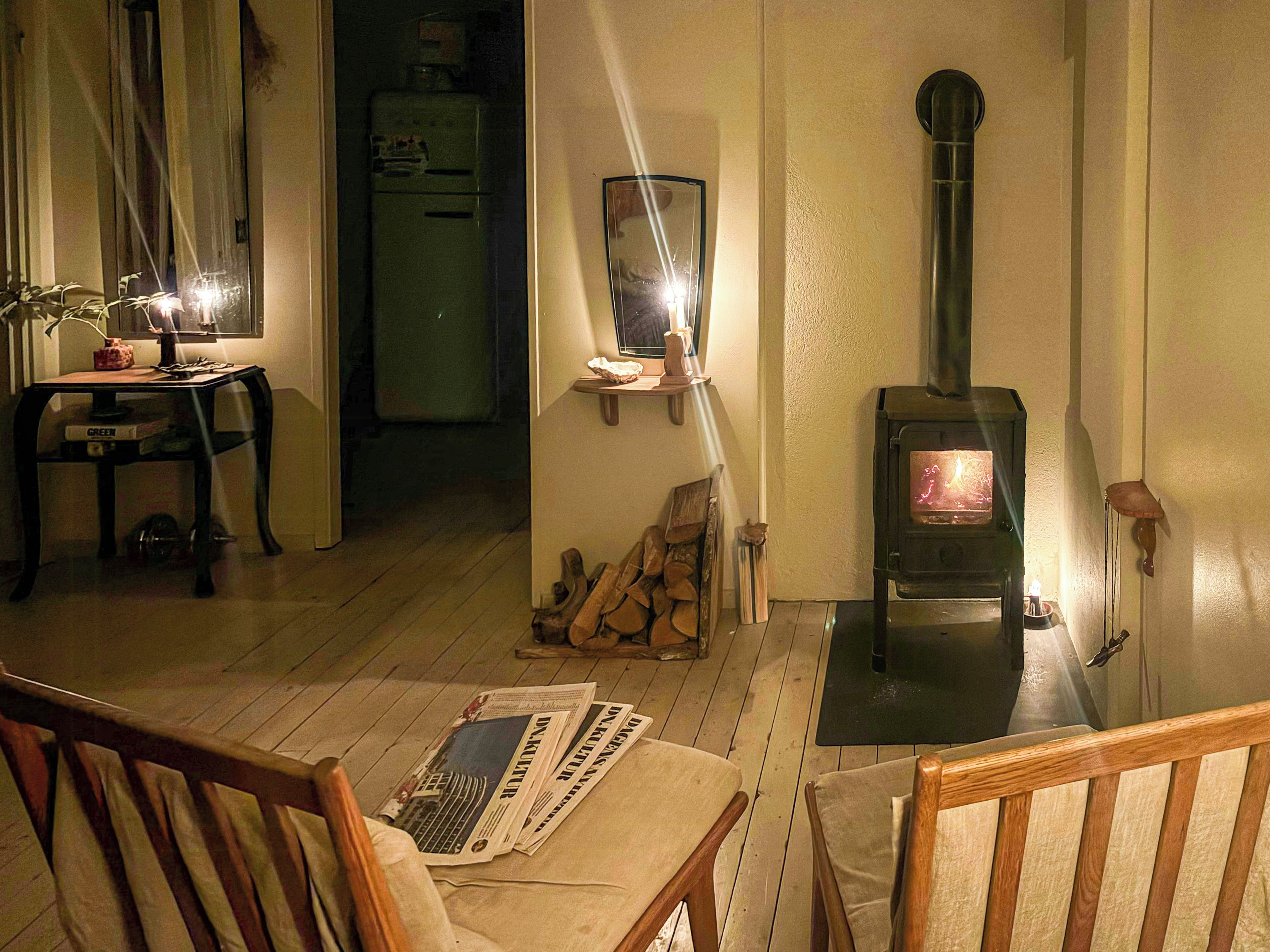 Een knusse woonkamer met een houten tafel, stoelen, een open haard en een spiegel aan de muur.