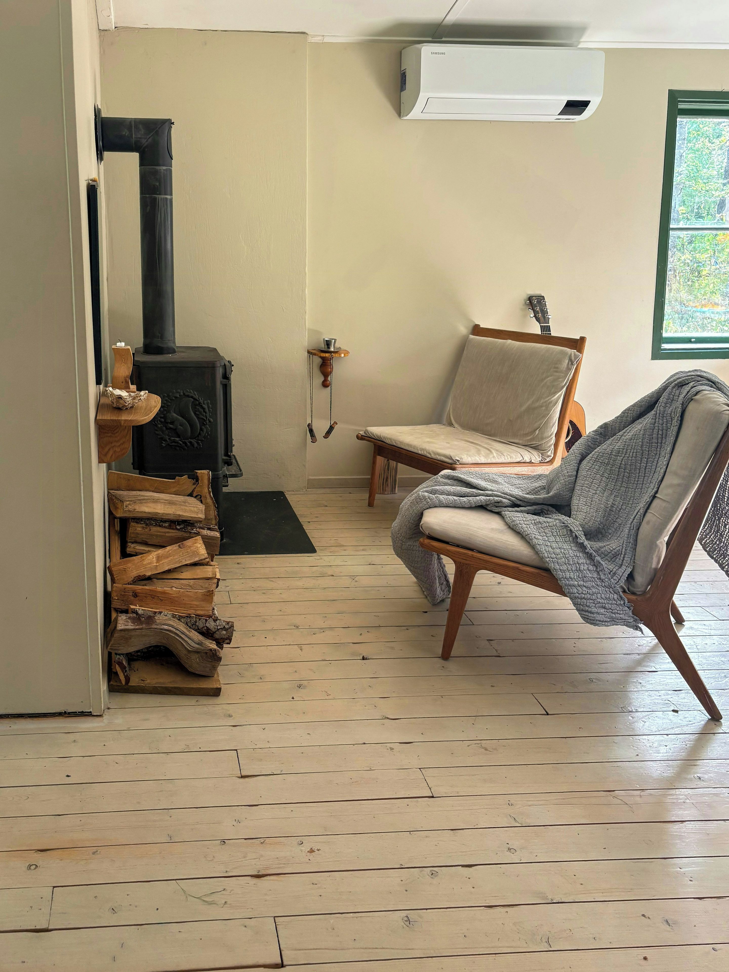 Ein Zimmer mit Kaminofen, Stuhl, Gitarre und einem Fenster mit Aussicht.