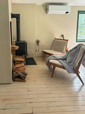 A room with a wood-burning stove, a chair, a guitar, and a window with a view.
