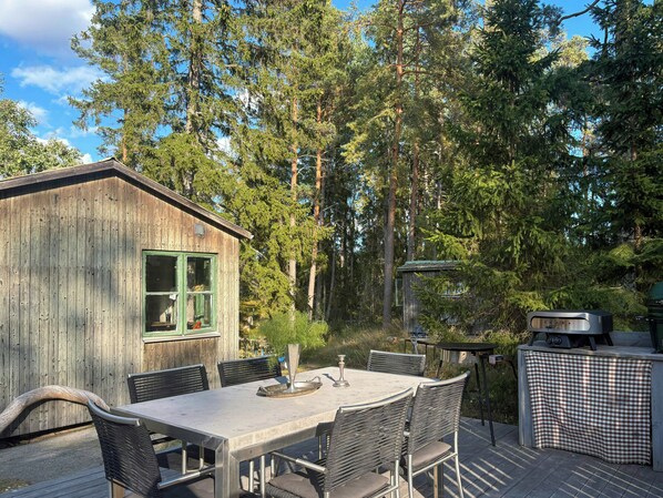 Eine Holzhütte mit Esstisch und Stühlen, umgeben von hohen Bäumen.
