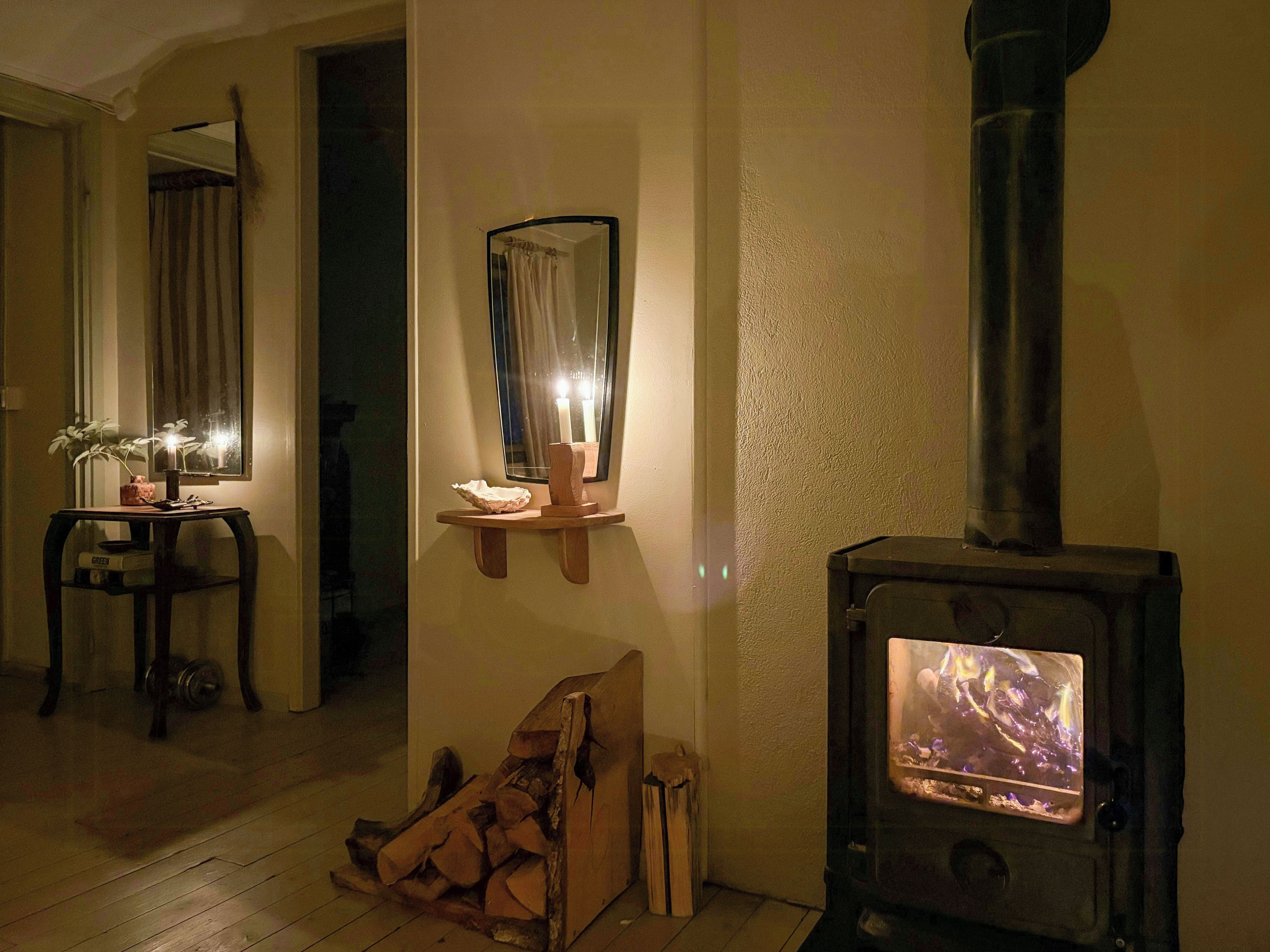 Een gezellige kamer met een houtkachel, een tafeltje met een plant en een spiegel aan de muur.