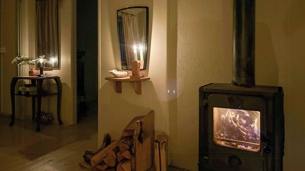 A cozy room with a wood-burning stove, a small table with a plant, and a mirror on the wall.