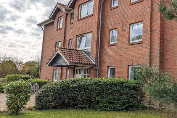 A multi-story brick building with a well-maintained garden and a bicycle parked outside. - Holiday apartment with 1 bedroom (Fehmarn)