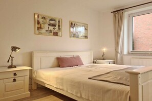A bedroom with a bed, bedside tables, a lamp, and two wall-mounted pictures. - Holiday apartment with 1 bedroom (Fehmarn)