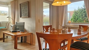 En matplats med ett träbord och stolar, en dator på ett skrivbord och ett fönster med gardiner.