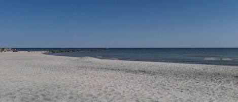 Une plage avec un ciel dégagé, une mer calme et un promontoire rocheux à l’horizon.