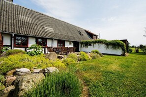 A traditional house with a sloped roof, a front porch with wooden chairs, and a garden with rocks and greenery. - Nydamsgaard "hus lille rede" (Faaborg \/ Bojden)