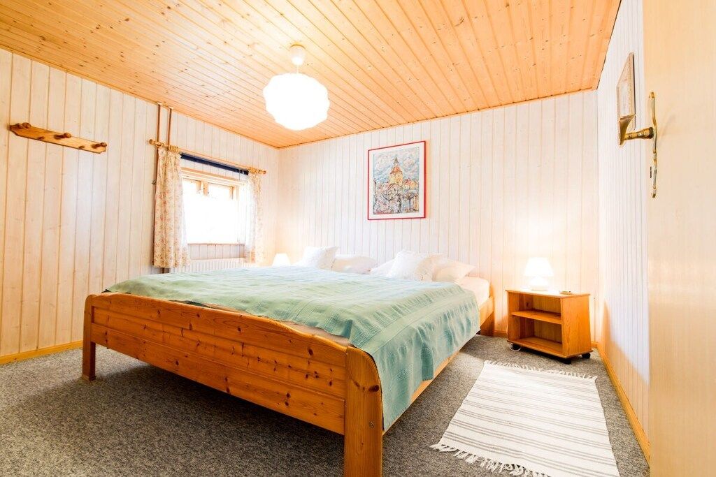 Een kamer met een houten bed, een nachtkastje, een lamp en een ingelijste foto aan de muur.