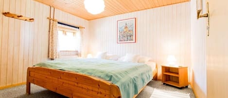 A room with a wooden bed, a nightstand, a lamp, and a framed picture on the wall.