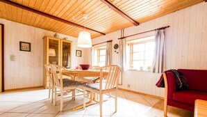 A room with a wooden ceiling, a dining table with chairs, a red sofa, and a window with curtains. - Nydamsgaard "hus lille rede" (Faaborg \/ Bojden)