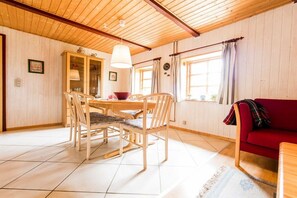 A room with a wooden ceiling, a dining table with chairs, a red sofa, and a window with curtains. - Nydamsgaard "hus lille rede" (Faaborg \/ Bojden)