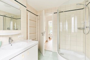 A bathroom with a glass-enclosed shower, a white sink, and a door leading to another room. - No. 2 - The Lake House (Walchensee)