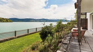 Eine Terrassensitzgruppe am Seeufer mit Blick auf Berge, einem Holzzaun und Gartenmöbeln.