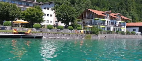 A lakeside hotel with outdoor seating, a pool, and buildings with balconies.