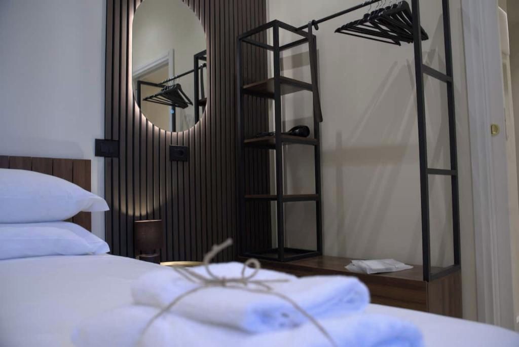 A neatly made bed with white linens, a hanging clothes rack, and a mirror on the wall.