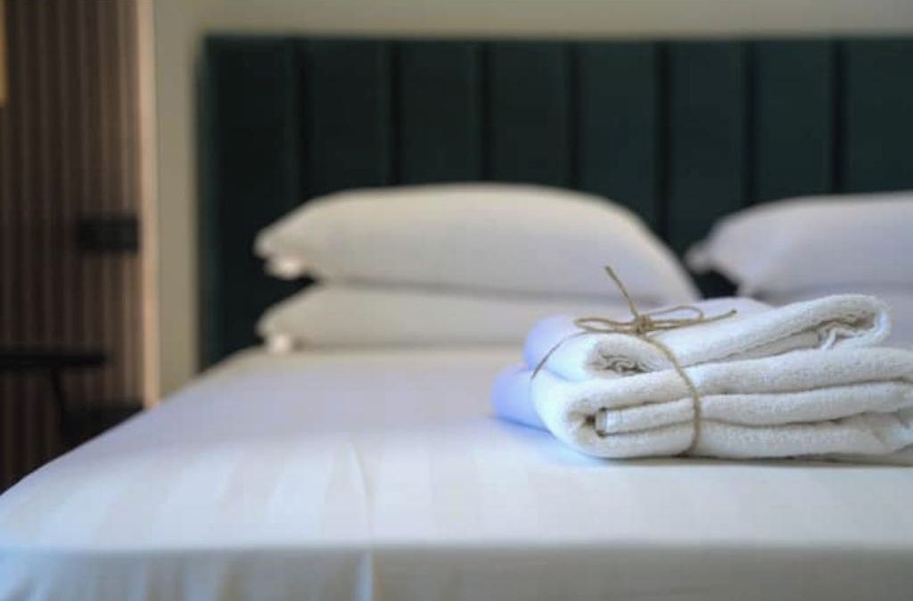 A neatly made bed with white linens and a folded towel on top.