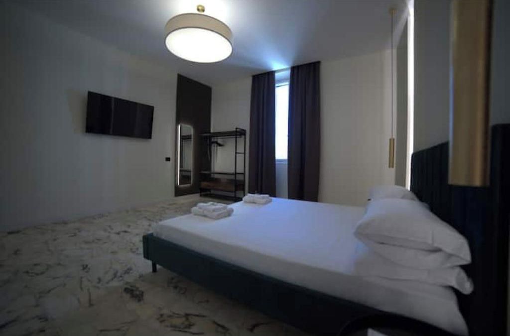 Une chambre d’hôtel équipée d’un lit, d’un téléviseur à écran plat, d’un miroir et d’une fenêtre avec des rideaux.