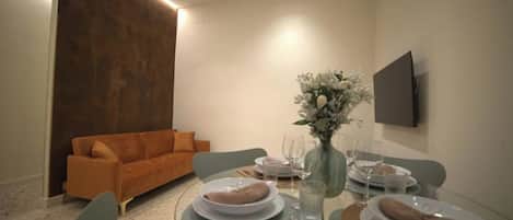 Un comedor con una mesa redonda dispuesta para cuatro personas, un sofá y un televisor montado en la pared.