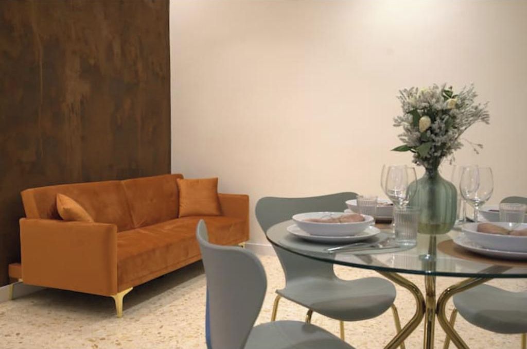 Un comedor con una mesa de vidrio, sillas grises, un sofá marrón y un jarrón con flores.