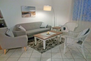 A living room with a sofa, armchairs, a coffee table, and a floor lamp. - Small holiday apartment Pappelhof (Fehmarn)