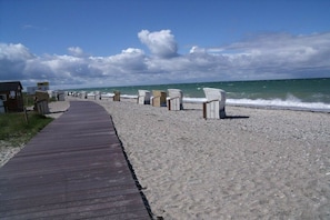 Ein hölzerner Steg führt zu Liegestühlen und einem kleinen Gebäude an einem Sandstrand.