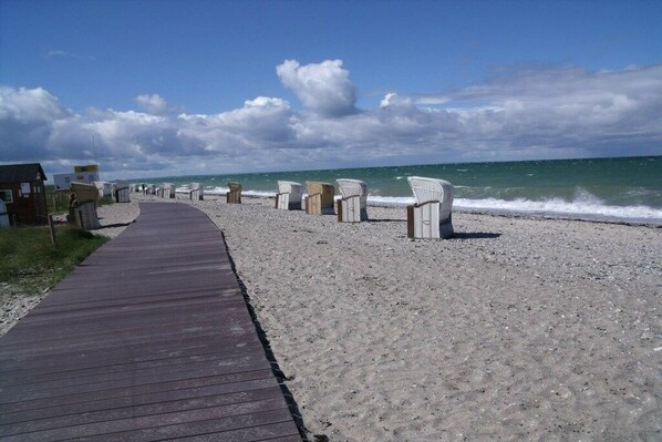 A wooden boardwalk leading to beach chairs and a small building on a sandy beach. - Small holiday apartment Pappelhof (Fehmarn)