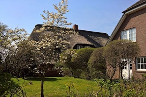 Ein traditionelles Backsteinhaus mit Strohdach und einem gepflegten Garten.