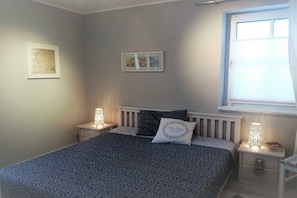 A bedroom with a bed, bedside tables, a window, and wall art. - Small holiday apartment Pappelhof (Fehmarn)