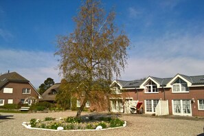 A row of houses with a central tree, gravel driveway, and a clear sky. - Small holiday apartment Pappelhof (Fehmarn)