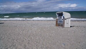 En strand med en ensam fåtölj av rotting som är placerad med ryggen mot havet.