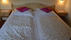 Cama de casal com roupa de cama florida e duas almofadas, com mesas de cabeceira laterais com abajures.