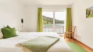 Ein Schlafzimmer mit einem Bett, einem Sessel, einem Fenster mit Vorhängen und einem Bild an der Wand.