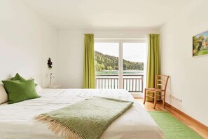 Ein Schlafzimmer mit einem Bett, einem Sessel, einem Fenster mit Vorhängen und einem Bild an der Wand.