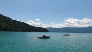 Un lago tranquilo con dos barcos, rodeado de colinas boscosas bajo un cielo despejado.
