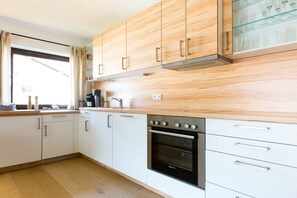 Eine moderne Küche mit weißen Schränken, einem eingebauten Backofen und einem Fenster mit Vorhängen.