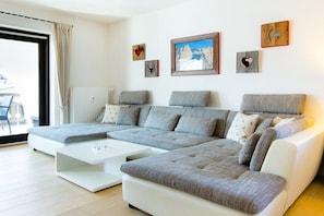 Un salon moderne avec un canapé d’angle, une table basse blanche et une grande fenêtre offrant une belle vue.