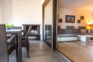 A living room with a fireplace, a sofa set, and a dining area with wicker furniture. - Holiday apartment with 2 bedrooms (Garmisch-Partenkirchen)