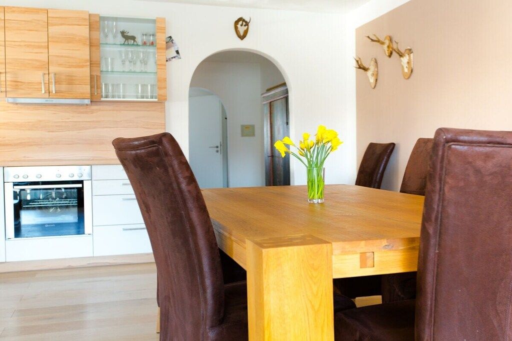 Un comedor con una mesa de madera, sillas tapizadas en tono café y un florero con flores amarillas.