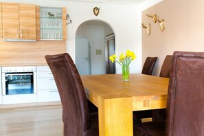 Un coin repas avec une table en bois, des chaises à revêtement marron et un vase rempli de fleurs jaunes.