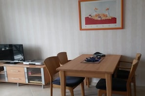A dining area with a wooden table and chairs, a television on a cabinet, and a framed picture on the wall. - Holiday apartment with 1 bedroom (Fehmarn)